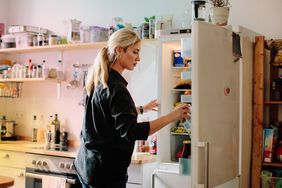 Una mujer adulta saca un cartón de leche del frigorífico de la cocina de casa.