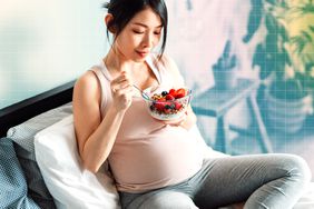 Mujer embarazada comiendo mientras está sentada en el sofá