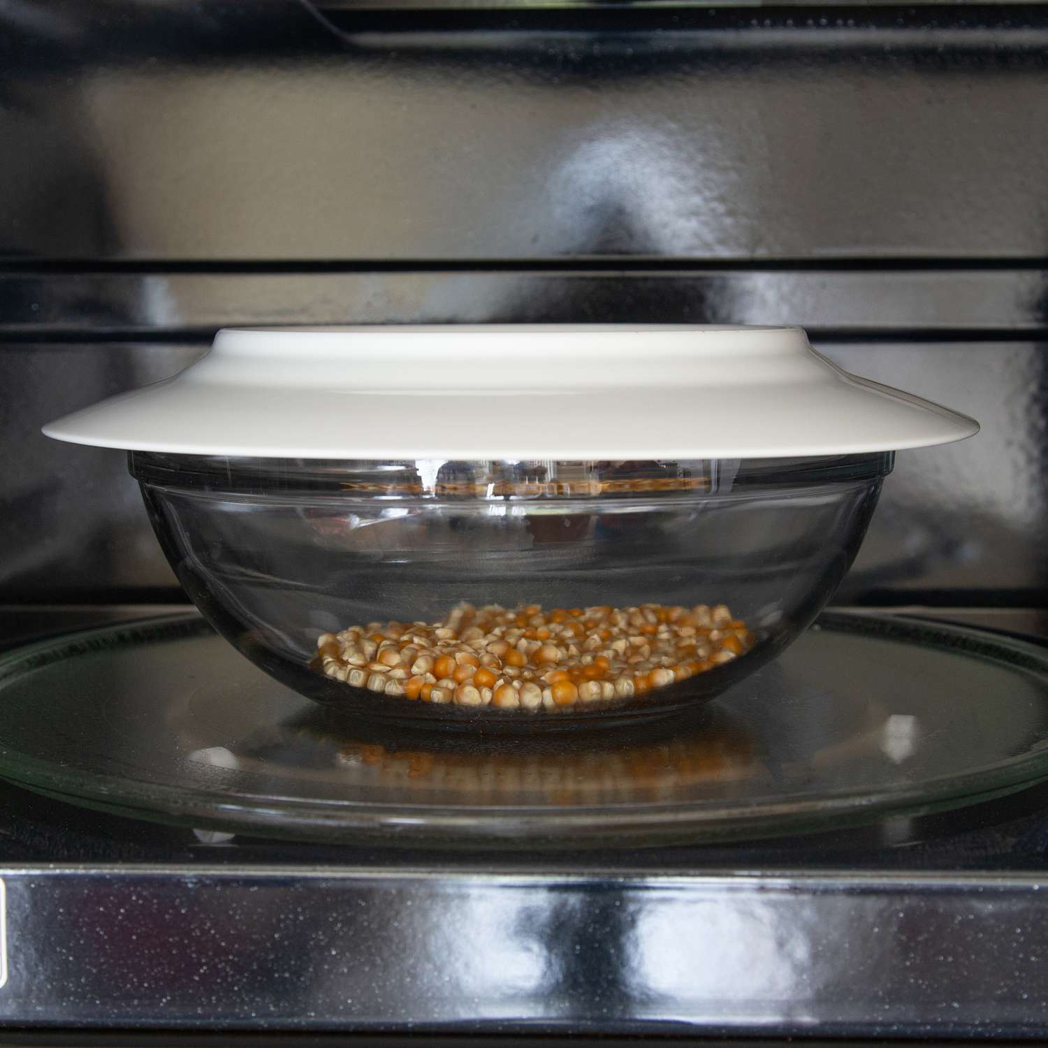 Manos para calentar la fruta de las palomitas de maíz en un tazón de vidrio en un plato blanco en un horno microondas.
