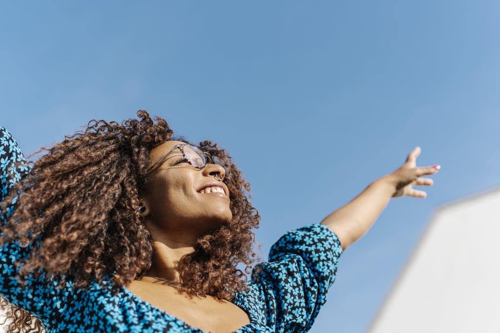 Una joven de raíces africanas levanta las manos contra el cielo azul. concepto de felicidad